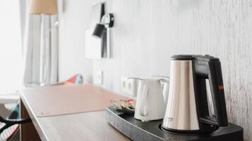A modern kitchen with a coffee maker, kettle, and a tray with cards on a wooden table.