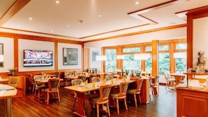 A spacious dining area with wooden tables and chairs, large windows, and a television mounted on the wall. - Hotel Hasselhof Garni 4 Sterne (Braunlage)