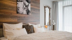 A bedroom with a wooden headboard, a deer painting, a mirror, and a fluffy white bedspread. - Hotel Hasselhof Garni 4 Sterne (Braunlage)