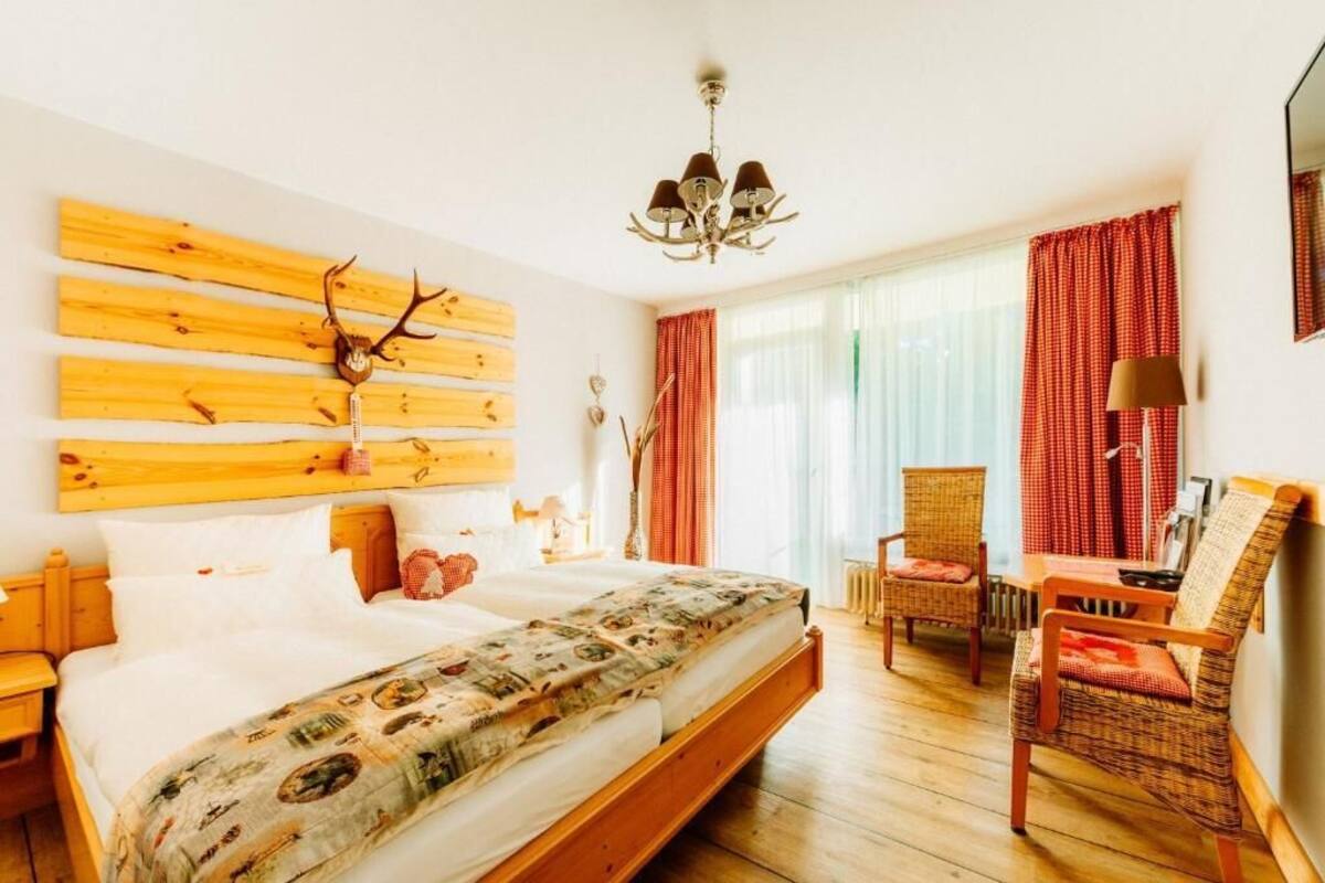 Une chambre avec un lit, une tête de lit en bois, un lustre, une fenêtre avec des rideaux et une chaise.