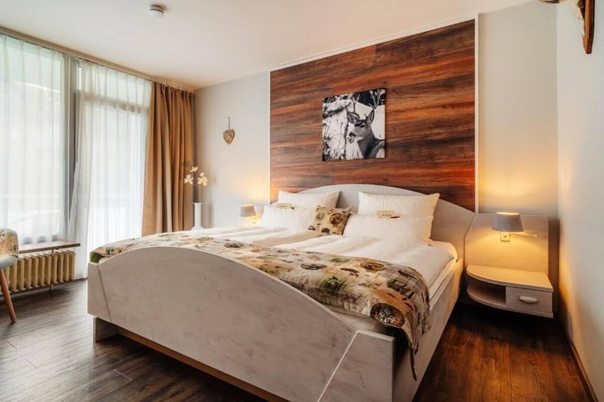 Une chambre d’hôtel moderne avec un grand lit, un mur décoratif en bois, un tableau encadré et une table de chevet avec une lampe.