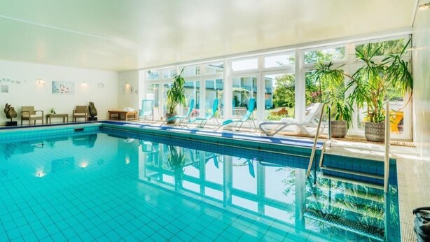 An indoor swimming pool with clear blue water, surrounded by lounge chairs and potted plants. - Hotel Hasselhof Garni 4 Sterne (Braunlage)