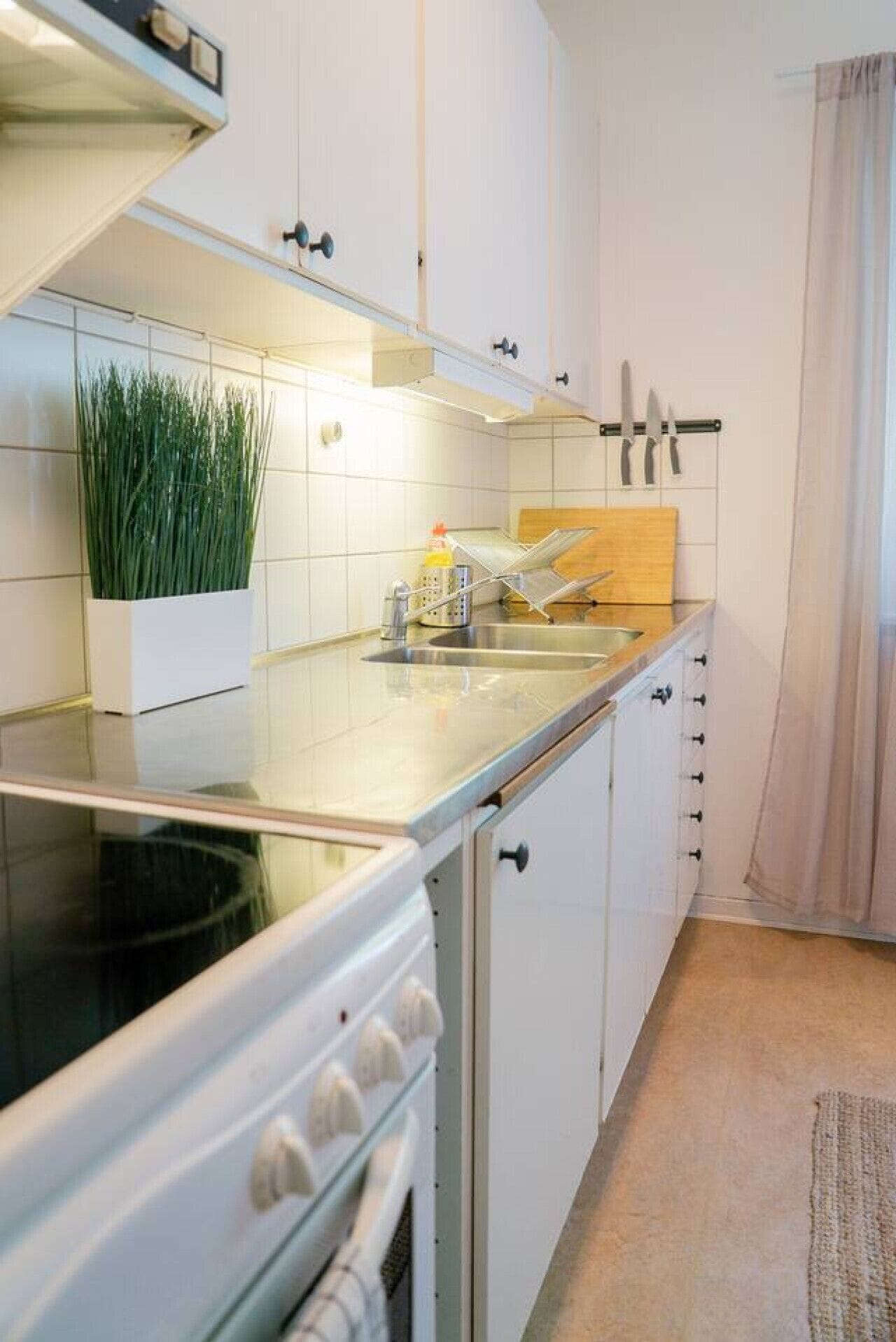 A compact kitchen with white cabinets, a stainless steel countertop, a built-in oven, and a small sink.