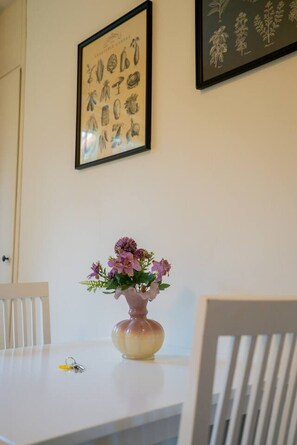 Ein Esstisch mit einer Blumenvase, einer gerahmten Pflanzenillustration und einem Schlüssel darauf.