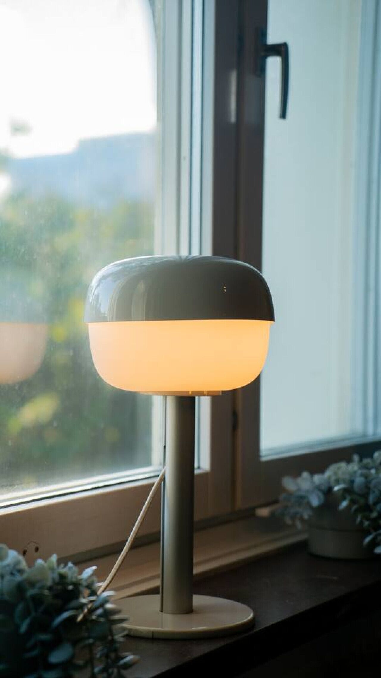 Una lampada moderna su un davanzale con vista su piante e spazi verdi.