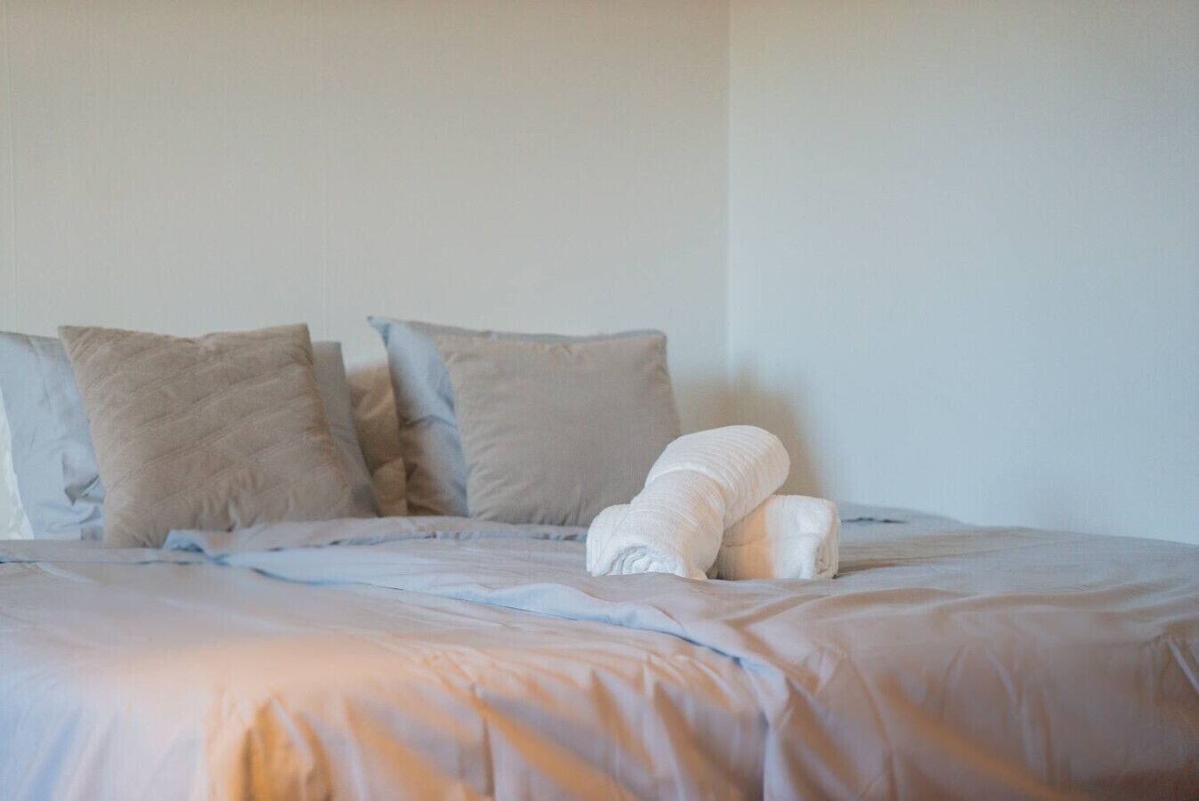 Un letto con una coperta bianca e cuscini, una parete spoglia e una finestra.