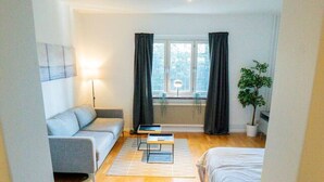 A modern, well-lit room with a sofa, a bed, a small table, and a potted plant. - Central Studio, Near City & Tram | Brämaregården (Gothenburg)