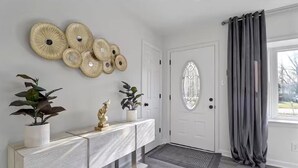 A hallway with a white door, a console table with plants, decorative wall art, and a grey curtain.