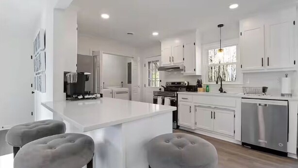 A modern kitchen with white cabinetry, a central island, bar stools, and stainless steel appliances.