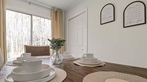 A dining room with a wooden table set for four, white plates, and a vase with greenery.