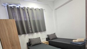 A room with two beds, a wooden wardrobe, and a curtain.