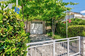 A stone pathway leading to a gated entrance, surrounded by lush greenery and a clear blue sky. - Vacation apartment near sandy beach with terrace, barbecue & parking space (Crikvenica)