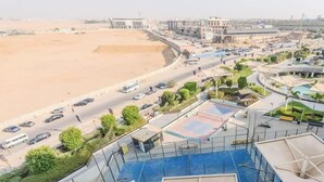 A view of a coastal area with a road, buildings, and a large sandy beach. - Luxury 2BR • Porto New Cairo • Pool & 3 Baths (New Cairo 1)