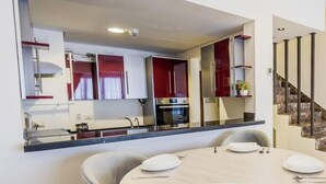 A modern kitchen with red cabinets, a built-in oven, and a dining area with a round table set for four. - Luxury 2BR • Porto New Cairo • Pool & 3 Baths (New Cairo 1)