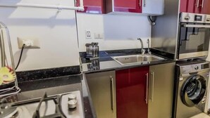 A compact kitchen with a gas stove, a sink, a microwave, and a washing machine. - Luxury 2BR • Porto New Cairo • Pool & 3 Baths (New Cairo 1)