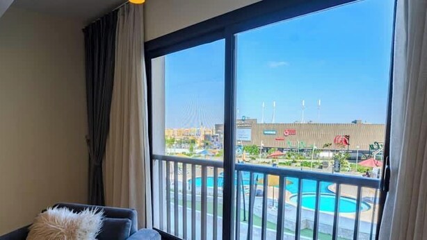 A room with a large window, a sofa, and a view of an outdoor swimming pool.