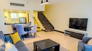 A living room with a sofa, coffee table, TV, and a staircase leading to a kitchen.