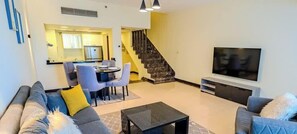 Un salon comprenant un canapé, une table basse, un téléviseur et un escalier menant à la cuisine.