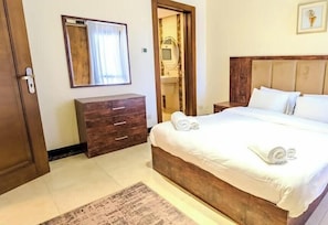 Une chambre à coucher avec un lit en bois, une table de chevet, une commode en bois, un miroir et une porte.