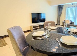 Un coin repas avec une table ronde dressée pour deux personnes, un téléviseur à écran plat fixé au mur et un canapé en arrière-plan.