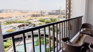 A balcony with a view of a residential area, a pool, and a building with a green roof. - Luxury 2BR • Porto New Cairo • Pool & 3 Baths (New Cairo 1)