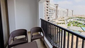 A balcony with two wicker chairs and a table, overlooking a residential area with high-rise buildings and a swimming pool. - Luxury 2BR • Porto New Cairo • Pool & 3 Baths (New Cairo 1)