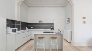 A modern kitchen with white cabinetry, a built-in microwave, a coffee maker, and a kettle. There are two stools at the island. - Tay Apartment (Edinburgh)