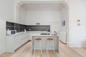 A modern kitchen with white cabinetry, a built-in microwave, a coffee maker, and a kettle. There are two stools at the island.