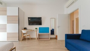 A modern room with a bed, a desk, a chair, a blue sofa, a TV, and a mirror. - Smart Arena Rooms - 10 minuti dall'Arena (Verona)