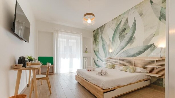 A bedroom with a bed, a desk, a chair, a television, and a large abstract wall painting. - Smart Arena Rooms - 10 minuti dall'Arena (Verona)