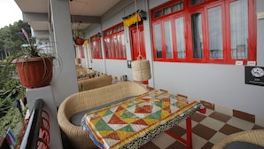A balcony with wicker furniture, a checkered floor, red-framed windows, and a hanging lantern. - Latitudee Boutique Rooms (Darjeeling)