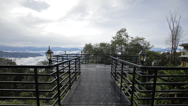 A wooden staircase leading to a viewpoint with metal railings and lanterns, surrounded by greenery and mountains in the distance. - Latitudee Boutique Rooms (Darjeeling)