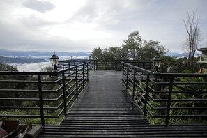 A wooden staircase leading to a viewpoint with metal railings and lanterns, surrounded by greenery and mountains in the distance. - Latitudee Boutique Rooms (Darjeeling)