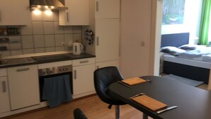 A compact kitchen with modern appliances, a dining table with a cutting board, and a view of a bed through a window. - Holiday Apartment for 2 Guests (63 m²) in Zittau (Zittau)