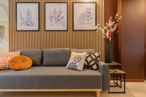 Un divano grigio con cuscini decorati, un vaso con fiori e alcuni schizzi blu incorniciati appesi al muro.