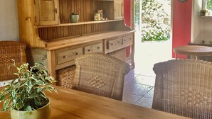 Zona pranzo con sedie in vimini, un mobiletto in legno con ripiani e una pianta in vaso.