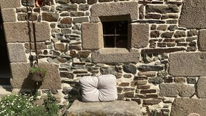 Un edificio in pietra con una finestra, una pentola appesa e un grande masso.