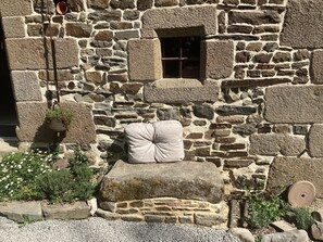 A stone building with a window, a hanging pot, and a large rock. - Charming vacation home near Mont-Saint-Michel in the countryside, centrally located (Brécey)
