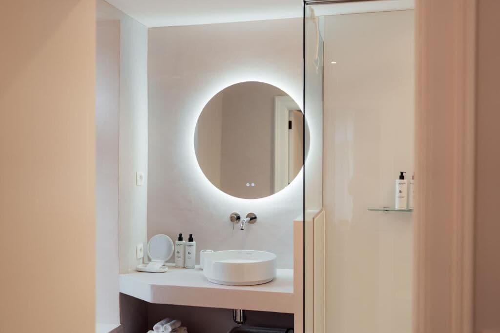 Een moderne badkamer met een ronde spiegel, een witte wastafel en een douchecabine van glas.