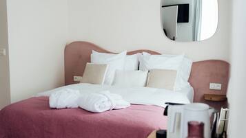 A neatly made bed with white and pink bedding, a bedside table with a lamp, and a mirror on the wall.