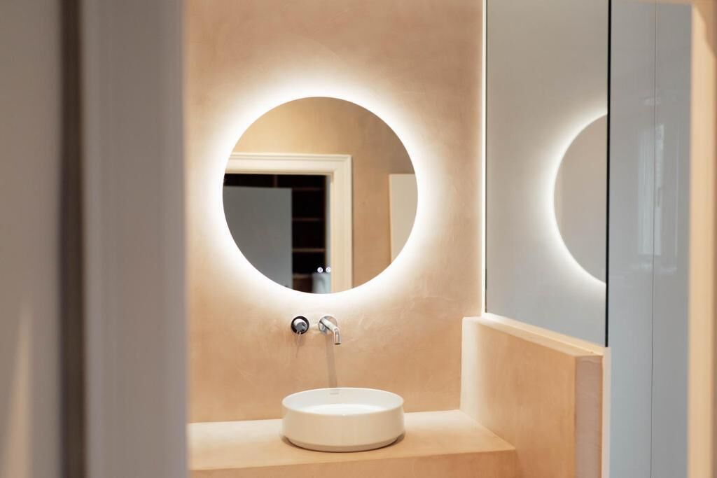 Een moderne badkamer met een ronde spiegel, een wastafel en een kastje.