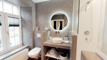Een moderne badkamer met een ronde spiegel, toilet, wastafel en douche.