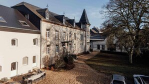 A historic building with a symmetrical facade, a central tower, and a courtyard with a car parked nearby. - Hotel Château Palacio (Fauvillers)