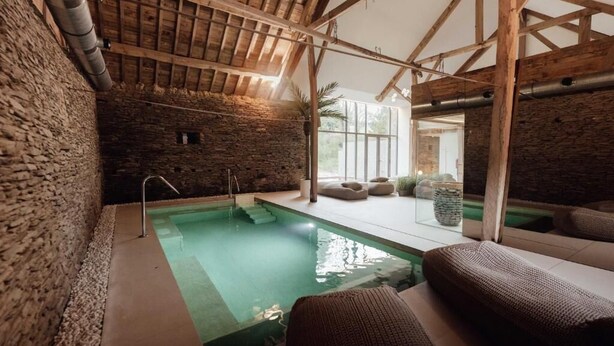 A spa area with a pool, stone walls, wooden beams, and seating. - Hotel Château Palacio (Fauvillers)