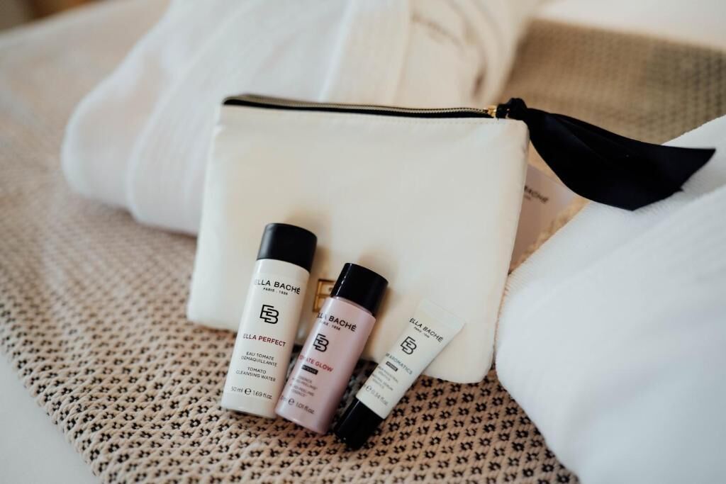 Une trousse de toilette blanche contenant trois produits : un flacon de produit de soin de la peau de la marque « ELLA BACHE », un tube de produit de soin de la peau de la marque « ELLA BACHE », et un petit flacon de produit de soin de la peau de la marque « ELLA BACHE ».