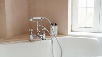 Un baño con bañera, cabezal de ducha y dos botellas de champú en un estante.