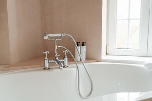 Un baño con bañera, cabezal de ducha y dos botellas de champú en un estante.