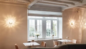 A dining area with a large window, two tables, and a sofa. - Hotel Château Palacio (Fauvillers)