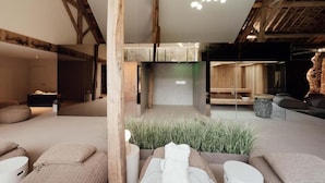 A modern interior with exposed wooden beams, a central seating area with cushions, and a hanging light fixture. - Hotel Château Palacio (Fauvillers)