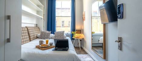 A bedroom with a bed, laptop, breakfast tray, and a TV on the wall.
